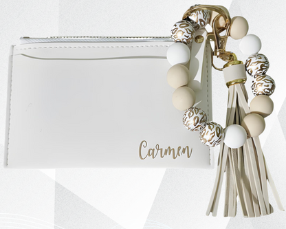 Bolso de mano blanco con un llavero decorativo con cuentas y borlas sobre fondo blanco.